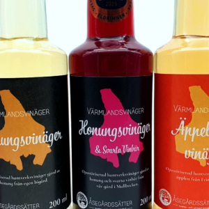 flera flaskor vinäger bredvid varandra. Från vänstertill höger. röd jordgubbsvinäger, ljusgul honungsvinäger, mörkröd honungsvinäger med svarta vinbär. Flaskan bär etiketten "svenska mästerskapen i mathantverk Eldrimner 2025 - Brons", ljusgul äpplecidervinäger, mörkbrun stoutvinäger.